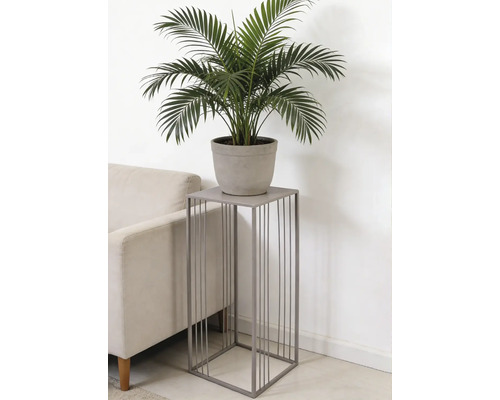 Vierkante plantenstandaard van grijs metaal met verticale spijlen, met een groene plant in pot naast een bank.