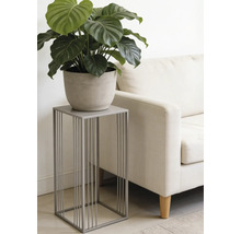 Moderne grijze metalen plantenstandaard met een minimalistisch ontwerp, met een groene plant in pot naast een lichte bank in een woonkamer.