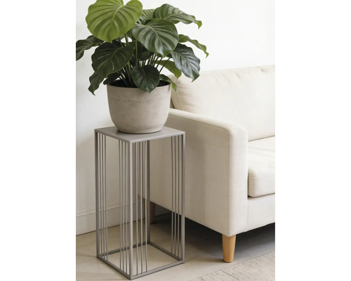 Moderne grijze metalen plantenstandaard met een minimalistisch ontwerp, met een groene plant in pot naast een lichte bank in een woonkamer.