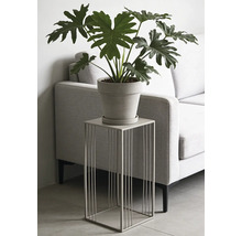 Moderne metalen plantenzuil met vierkant draadframe, voorzien van een plant in pot, in een woonkamer naast een bank.
