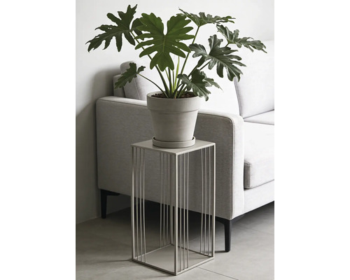 Moderne metalen plantenzuil met vierkant draadframe, voorzien van een plant in pot, in een woonkamer naast een bank.