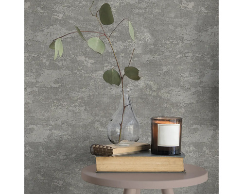 Vliesbehang in grijze betonlook met structuur, gedecoreerd met vaas, eucalyptustak en kaars op een bijzettafeltje.