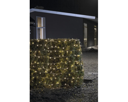 Warmwitte LED-lichtketting voor buiten, gewikkeld om een haag, bij nacht in een tuin voor een huis.