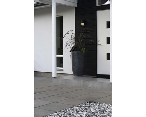 Moderne entree met hoge antracietkleurige plantenbak, siergras en grijze terrastegels.