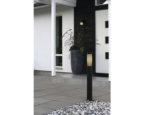 Moderne buitenverlichting met zwarte sokkelamp en bijpassende wandlamp bij de entree met plantenbak en terrastegels.