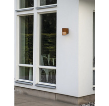Rechthoekige buitenwandlamp met roestlook op een gevel naast grote ramen.