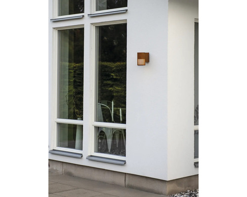 Rechthoekige buitenwandlamp met roestlook op een gevel naast grote ramen.