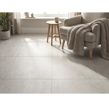 Grootformaat vloertegels in betonlook in een lichte woonkamer met fauteuil, gebreide deken en houten bijzettafel.