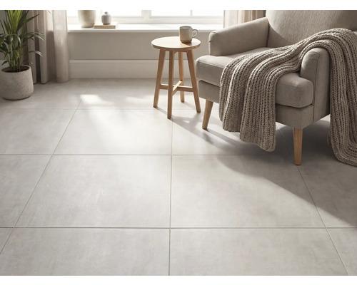 Grootformaat vloertegels in betonlook in een lichte woonkamer met fauteuil, gebreide deken en houten bijzettafel.