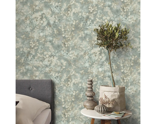 Vliesbehang met bloemenpatroon in vintagestijl in de slaapkamer achter een grijs gestoffeerd bed en een bijzettafel met olijfboom.