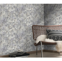 Vliesbehang met floraal patroon in grijstinten in een moderne kamer met vlechtstoel en lichte houten vloer.