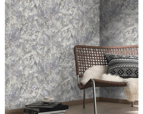 Vliesbehang met floraal patroon in grijstinten in een moderne kamer met vlechtstoel en lichte houten vloer.