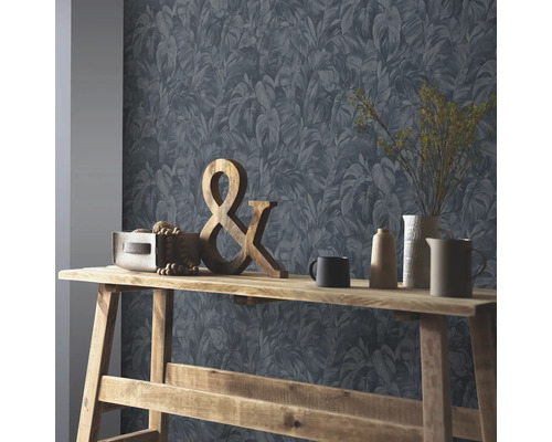 Vliesbehang met tropisch bladmotief achter een houten consoletafel met een ampersand en verschillende vazen.