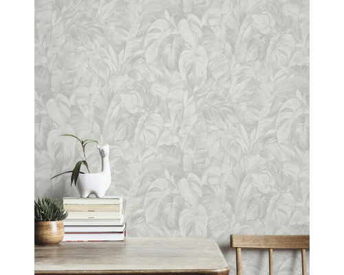 Lichtgekleurd behang met tropisch bladerpatroon van monstera- en palmbladeren achter een houten tafel met kamerplanten.