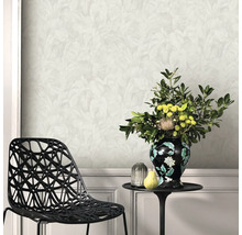 Woonkamer met lichtgekleurd behang met bladmotief, een zwarte geometrische stoel en een bijzettafel met bloemenvaas.