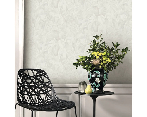 Woonkamer met lichtgekleurd behang met bladmotief, een zwarte geometrische stoel en een bijzettafel met bloemenvaas.