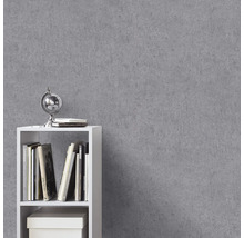 Vliesbehang met betonlook op een muur naast een witte kast met boeken.