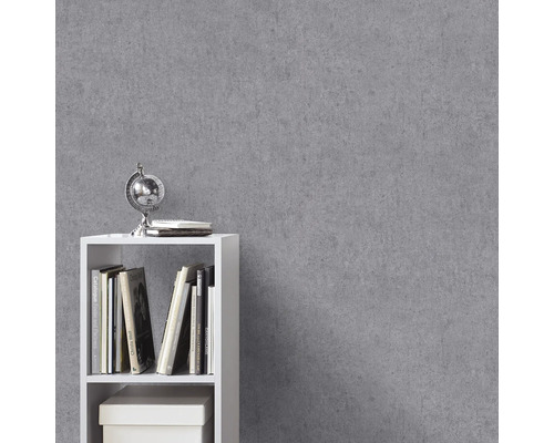 Vliesbehang met betonlook op een muur naast een witte kast met boeken.