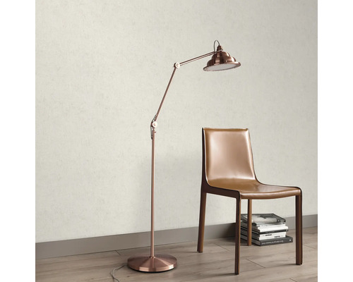 Licht gestructureerd behang in een kamer met een koperkleurige vloerlamp en een bruine lederen stoel op een vloer met houtlook.