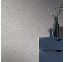 Vliesbehang met gestructureerde betonlook op een muur achter een blauwe ladekast met vazen in een moderne kamer.
