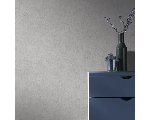Vliesbehang met gestructureerde betonlook op een muur achter een blauwe ladekast met vazen in een moderne kamer.