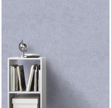 Gestructureerd vliesbehang in lila met pleisterlook op een muur achter een witte kast met boeken en een globe.
