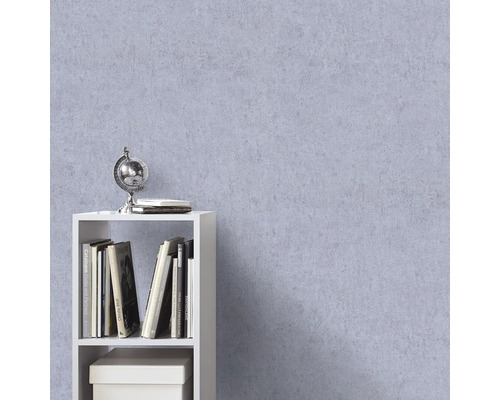 Gestructureerd vliesbehang in lila met pleisterlook op een muur achter een witte kast met boeken en een globe.