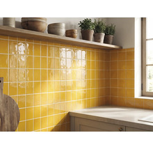 Keukenachterwand met gele glanzende vierkante wandtegels, een houten plank met schalen en kruiden en een aanrechtblad.