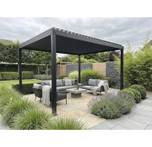 Moderne aluminium lamellenoverkapping boven een zithoek met grijze tuinmeubelen op een stenen terras, omringd door beplanting.
