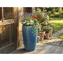 Hoge blauwe keramieken plantenbak met lavendel en geraniums op een houten terras naast een houten tuinhuis.