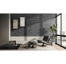 Moderne woonkamer met steenstrips in grijze baksteenlook, een fauteuil met voetenbank, een groot raam en een kamerplant.