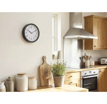 Lichte keuken met een ronde wandklok aan de muur, houten snijplank, kruidenpot en voorraadpotten op het aanrecht.