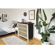 Moderne ladekast met drie laden in rotan look, wit frame en zwart bovenblad in een lichte slaapkamer met houten vloer.