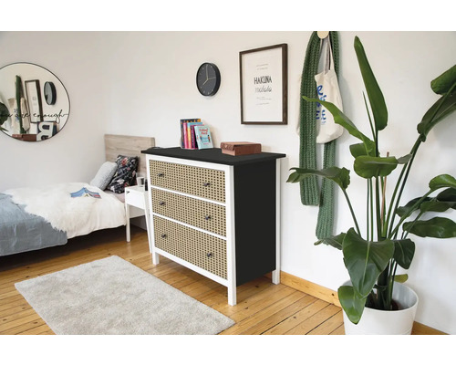 Moderne ladekast met drie laden in rotan look, wit frame en zwart bovenblad in een lichte slaapkamer met houten vloer.