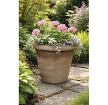 Grote, beplante bloempot van terracotta met roze, witte en paarse bloemen op een licht stenen pad in een lichte, groene tuin.
