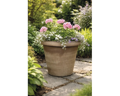 Grote, beplante bloempot van terracotta met roze, witte en paarse bloemen op een licht stenen pad in een lichte, groene tuin.