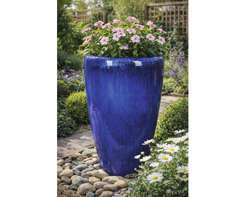 Hoge, blauw geglazuurde keramische bloempot met roze bloemen in een tuin met kiezels.