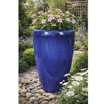 Hoge, blauw geglazuurde keramische bloempot met roze bloemen in een tuin met kiezels.
