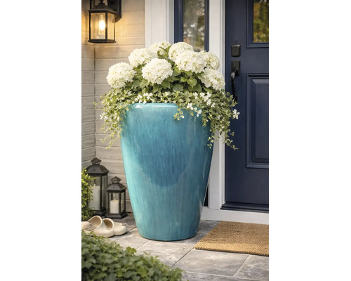Grote, blauw geglazuurde keramische plantenpot met witte hortensia's en hangplanten bij een donkere voordeur.
