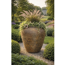 Grote getextureerde plantenpot van keramiek in een tuin, beplant met siergrassen en bloemen op een grindpad.