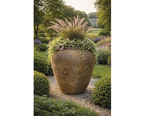 Grote getextureerde plantenpot van keramiek in een tuin, beplant met siergrassen en bloemen op een grindpad.