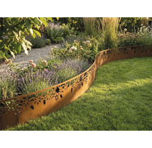 Decoratieve gazonrand van metaal in roestoptiek met bloemenpatroon scheidt een plantenperk van een gazon in een lichte tuin.