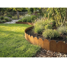 Gegolfde gazonrand van metaal in roestlook scheidt een plantenborder van een gazon in een lichte tuin.
