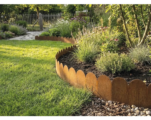 Gegolfde gazonrand van metaal in roestlook scheidt een plantenborder van een gazon in een lichte tuin.