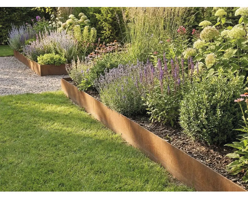 Borderrand van cortenstaal scheidt het gazon van een bloembed met grassen en vaste planten.