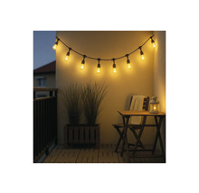 Lichtsnoer met led-lampen op een balkon met houten meubels en plantenbak in de avond.