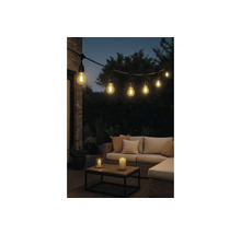 Lichtsnoer voor buiten met brandende lampen boven een loungeset met kussens, houten tafel en kaarsen in de avond.