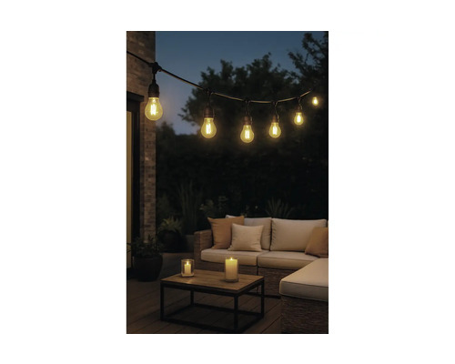 Lichtsnoer voor buiten met brandende lampen boven een loungeset met kussens, houten tafel en kaarsen in de avond.