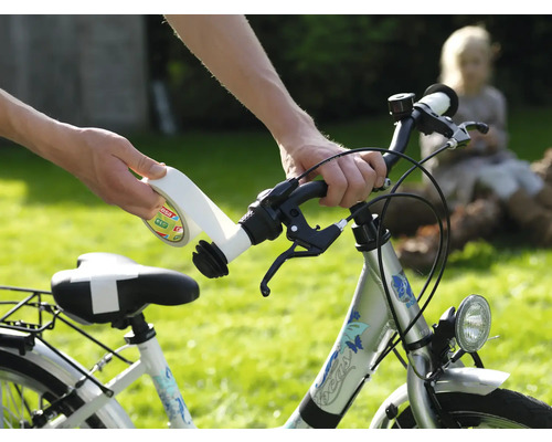 Handen plakken wit plakband met tesa Logo op het stuur van een zilveren kinderfiets in een lichte tuin.