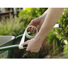 Iemand wikkelt witte tape om de handgreep van een groene kruiwagen in de tuin ter reparatie.